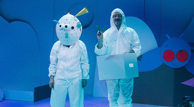 Two performers wear white costumes in a performance of Creation Creation. One performer wears a large white mask while the other had a white box around their torso. 